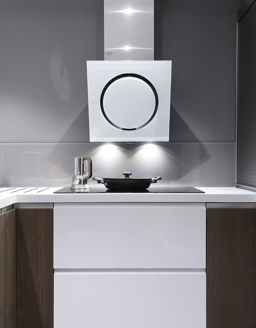 A modern kitchen with a sleek white and stainless steel range hood, a glass backsplash, and a minimalist cooktop. Dark wood cabinetry contrasts with glossy white drawers for a contemporary look.