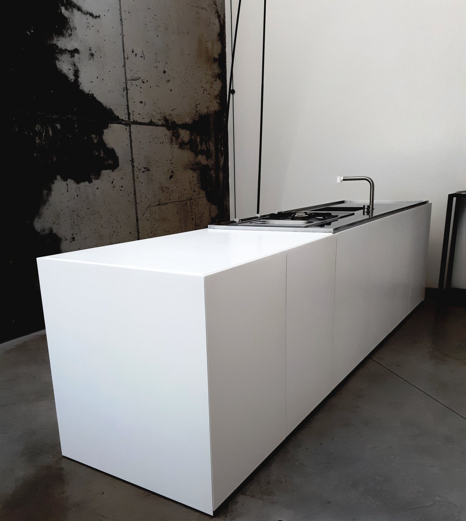 A minimalist kitchen island with a sleek, all-white design. The island features a clean, modern look with sharp lines and a built-in stainless steel faucet and cooktop.