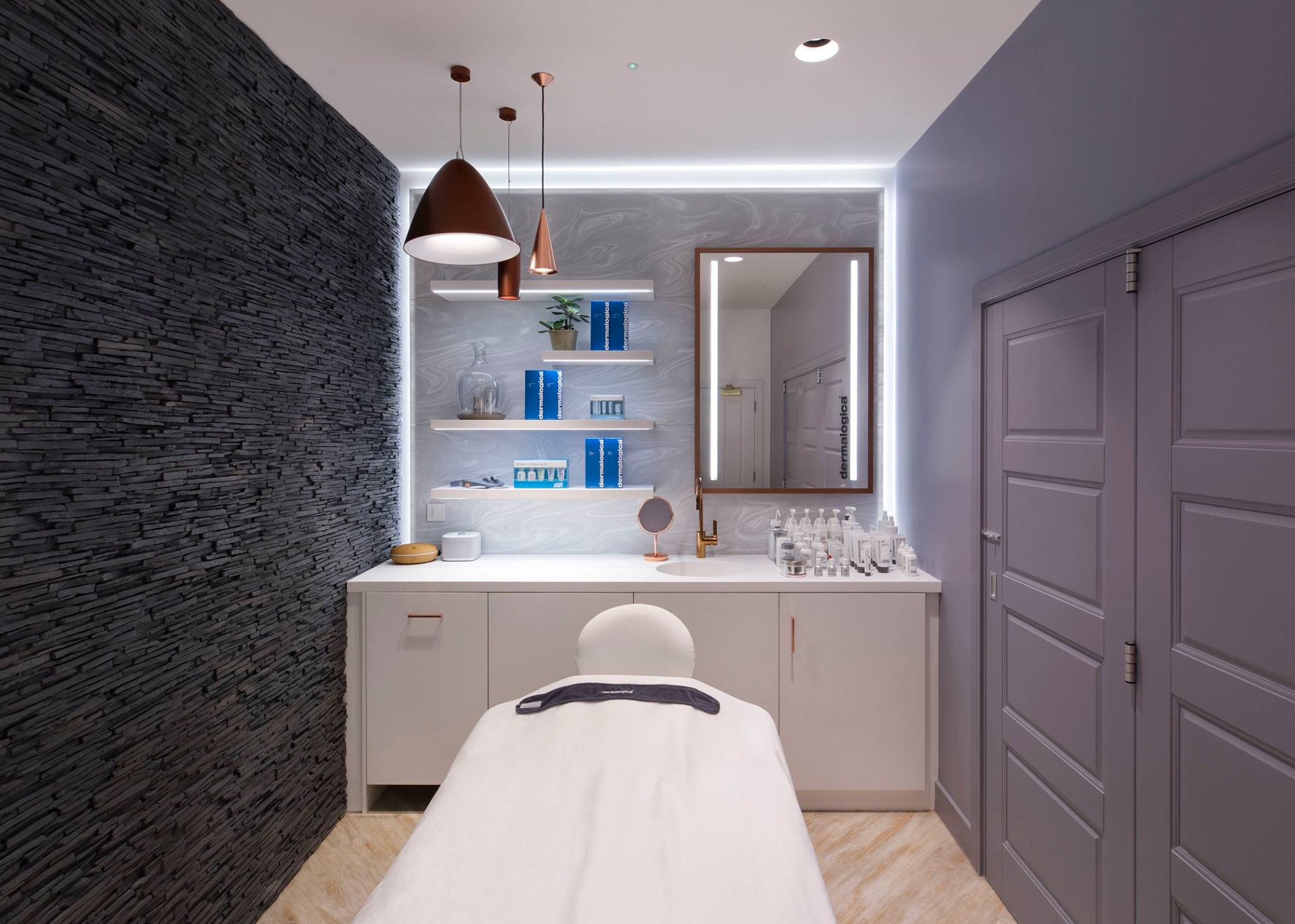Modern spa room featuring a treatment bed facing a sleek vanity area with open shelving.