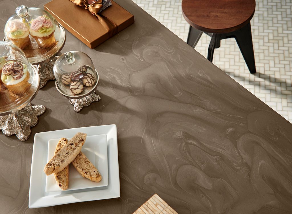 Brown marbled countertop with glass cloches holding cupcakes, chocolates, and a plate of biscotti.