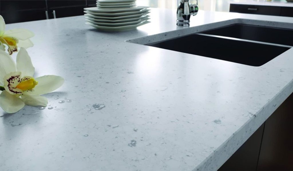A white countertop with deep sinks, and stacked plates and fresh flowers on the countertop.