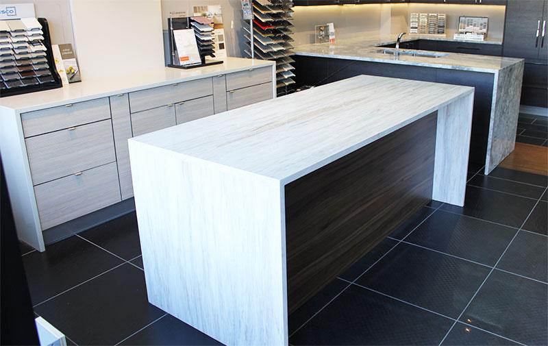 Modern kitchen featuring a large white island with a wooden side panel, gray cabinetry, and a granite countertop in the background.