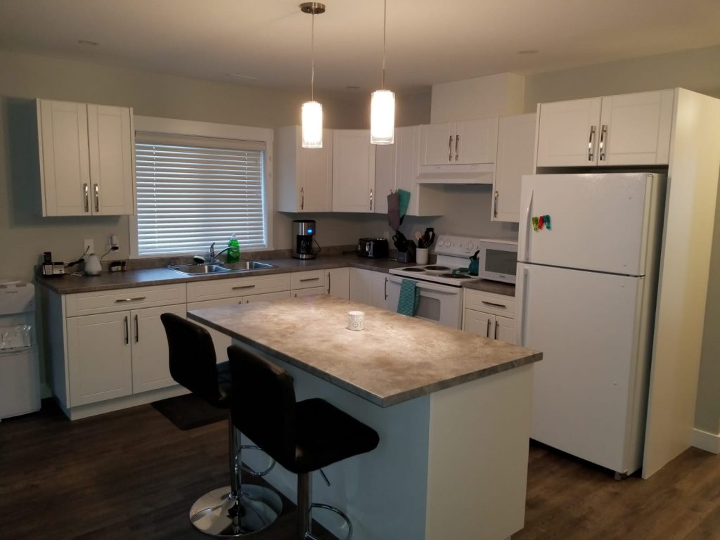 Modern kitchen with white cabinets, gray countertops, a center island, stainless steel sink, and white appliances.