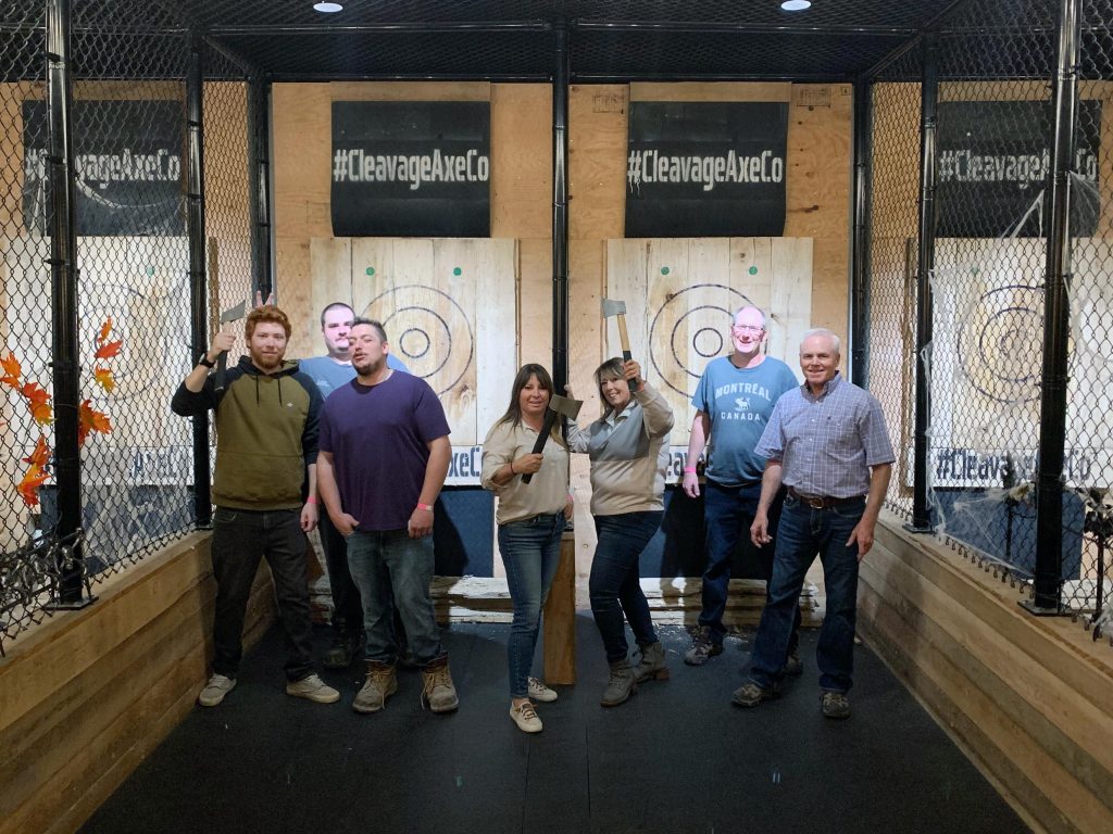 Group enjoying axe throwing at Cleavage Axe Company, posing with axes and smiling for a team-building event.