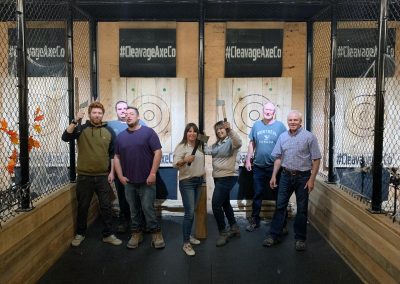 Group enjoying axe throwing at Cleavage Axe Company, posing with axes and smiling for a team-building event.